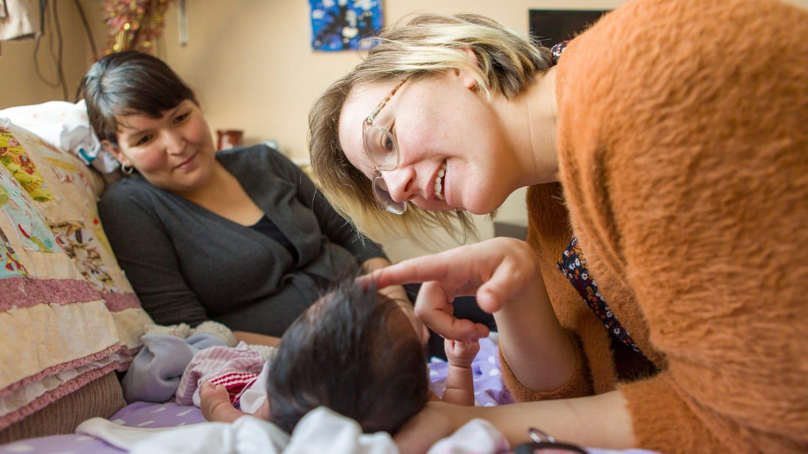 Photo of a midwife examining a baby as the child’s mother watches.